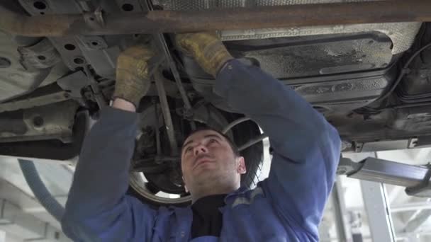 Auto technique resserre la suspension et les pièces de la machine dans le fond de la voiture, soulevant la voiture au-dessus du sol dans l'atelier de service de voiture — Video