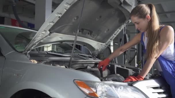 Hezká dívka v uniformě ukazuje šroubovák v motoru automobilu. Auto servis, opravy, údržbu a lidé koncept - mechanik žena pracující v dílně. — Stock video
