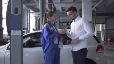 Araba muayene için hakkında verileri almak ve dostu araba hizmetinde bir istemci tarafından elini sıkarken genç kadın otomobil uzmanı