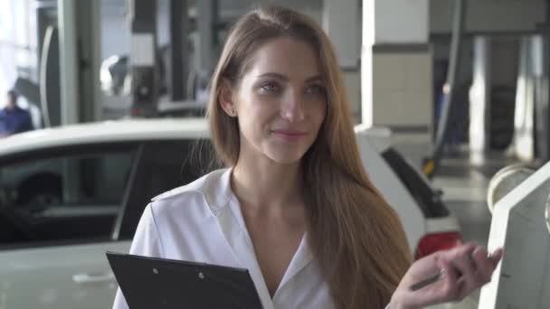Junge glückliche Frau im Autoservice zeigt ihren Autoschlüssel, lächelt und jubelt auf dem Hintergrund ihres Autos — Stockvideo