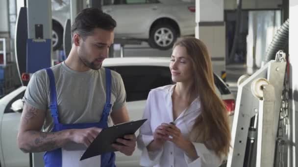 Auto servis, opravy, dohodu a lidé koncept - mechanik a zákazník nebo auto majitel podpisu papíru potřesení rukou v dílně. Sladký usmívající se dívka dává jí klíče od auta do krásné auto mechanik. — Stock video