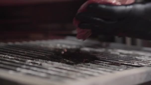그릴에 갈비와 고기 검은 장갑은 조각에 요리사의 손 닫습니다. 요리사는 그릴에 신선한 육즙 고기를 넣습니다. 슬로우 모션입니다. 현대적인 레스토랑에서 음식을 준비의 개념 — 비디오