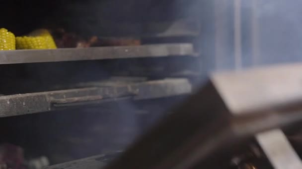 Chef en guantes negros abriendo la parrilla del horno, en el que se prepararon costillas fritas, maíz y verduras. De cerca. — Vídeos de Stock
