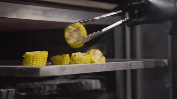 Chef en guantes negros convierte en horno caliente a la parrilla trozos de maíz en rodajas para freírlos por todos lados. De cerca. — Vídeo de stock