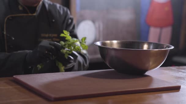 Figura borrosa de chef rasga hojas de perejil y pone en el tazón de aluminio grande de cerca. Preparación de comida en un restaurante moderno — Vídeo de stock