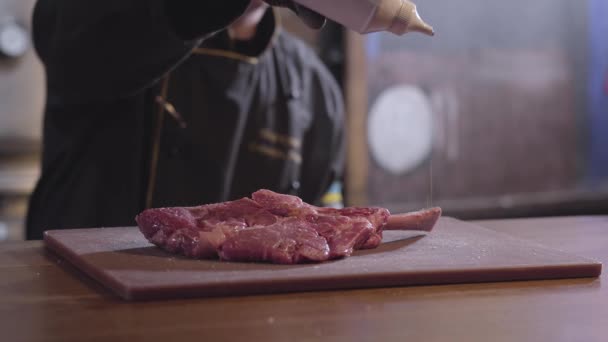 Koch gießt Stück Fleisch mit Knochen mit Sirup auf beiden Seiten aus nächster Nähe. Köchin in schwarzem Gewand und Gummihandschuhen. Zubereitung von Essen im Restaurant — Stockvideo