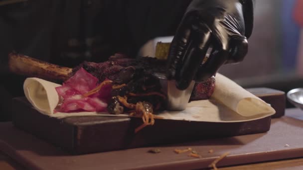 Шеф-повар в черных перчатках, подающий на тарелке мясо на гриле, нарезанные куски жареной кукурузы, соусы и имбирь. Закрыть — стоковое видео