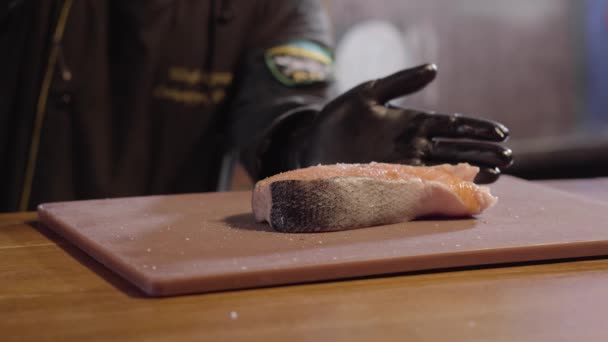 Руки шеф-кухаря наливають великий шматочок лосося з сиропом крупним планом. Чоловік у чорному халаті та гумових рукавичках готує тарілку. Готуємо їжу в ресторані — стокове відео