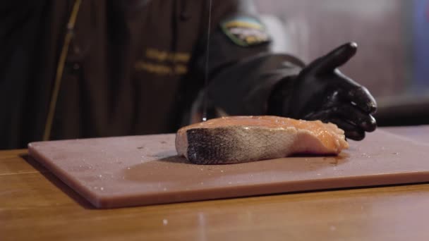 Les mains du chef versent un gros morceau de saumon avec de l'huile à proximité. Homme en robe noire et gants en caoutchouc plat de cuisson. Préparation de la nourriture au restaurant — Video