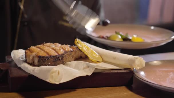 厨师的手把烤石灰和柠檬片附近的大一块美味的三文鱼在皮塔使用钳子关闭。在餐厅准备和供应食物 — 图库视频影像