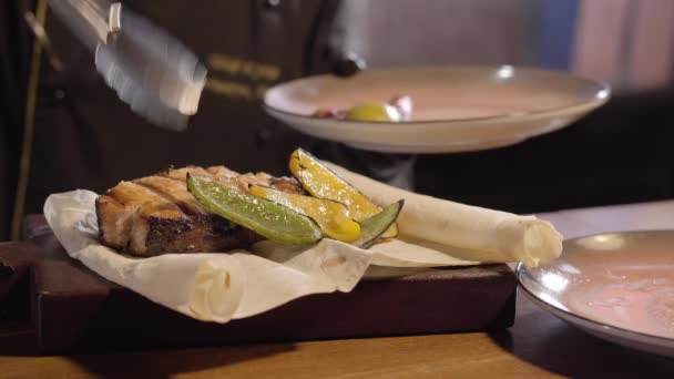 シェフはグリル、胡椒を入れてトングを使用してピタおいしい鮭魚の大きな部分の近くのレモン スライスをクローズ アップ。レストランで料理の準備と. — ストック動画
