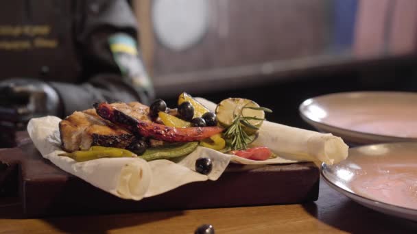 Close-up van de hand van een chef-koks in zwarte rubber koks handschoenen zetten van verse rozemarijn en citroen bladeren op een plaat met een heerlijk sappige gegrilde stuk vis en segmenten van geroosterde paprika, citroen en limoen. — Stockvideo