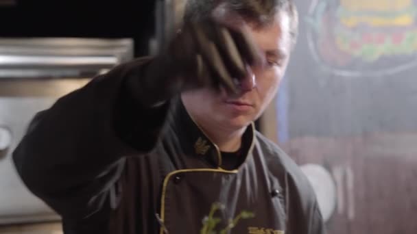 Portret van chef-kok in zwarte handschoenen dienen en zout op een bureau gegrilde vis, gesneden stukjes paprika, olijven en kalk. Close-up — Stockvideo