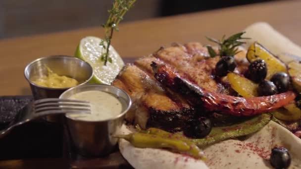 Pescado de salmón a la parrilla servido con salsas, hierbas, aceitunas, chile, lima y limón acostado en pita de cerca. Preparar y servir comida en un restaurante — Vídeos de Stock