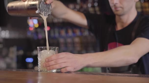 Barman verter cóctel de huevo de agitador de metal en vaso con hielo, girándolo en círculo. Joven haciendo sabroso cóctel en el bar — Vídeo de stock
