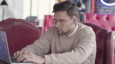Modern kafede dizüstü bilgisayar ile çalışan yakışıklı erkeğin kapatın. Şık emin işadamı vücudunu müziğin ritmine taşır. Projede çalışan olumlu serbest meslek