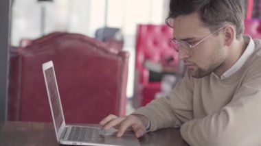 Modern kafede dizüstü bilgisayar ile çalışan yakışıklı erkeğin kapatın. Şık emin iş adamı problem çözme hakkında düşünme. Projede çalışan ciddi serbest meslek. Kamera sağa taşır