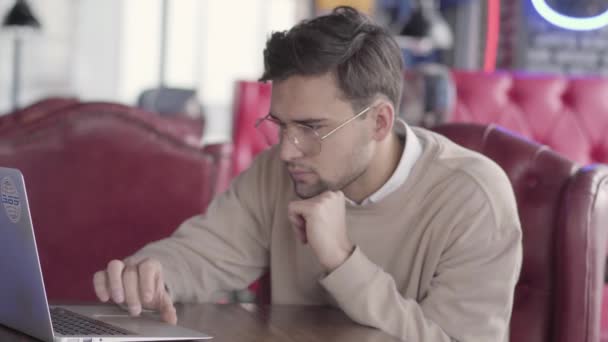 Stilig Fundersam Man Med Glasögon Tittar Bärbar Dator Medan Sitter — Stockvideo