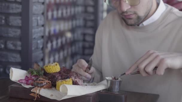 Chico guapo sentado en un restaurante de lujo y comiendo un delicioso plato impresionante con carne y verduras a la parrilla — Vídeos de Stock