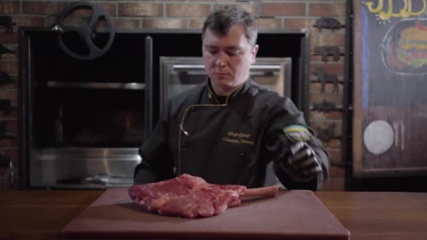 Chef-kok legt een rauwe, sappig stuk vlees op een snijplank en zouten van het aan alle kanten terwijl je in de keuken van het restaurant. — Stockvideo