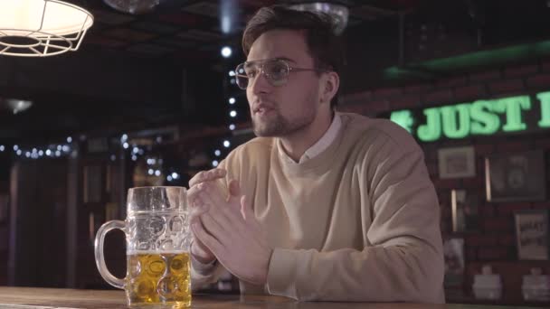 Відвідувач бару сидить за баром, п'є пиво і емоційно дивиться футбольний матч після робочого дня — стокове відео