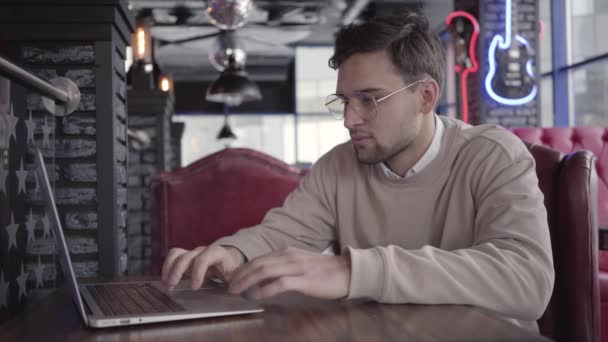 Красивый человек, работающий с ноутбуком в современном кафе крупным планом. Стильный уверенный бизнесмен думает о решении проблемы. Серьезный фрилансер, работающий над проектом — стоковое видео