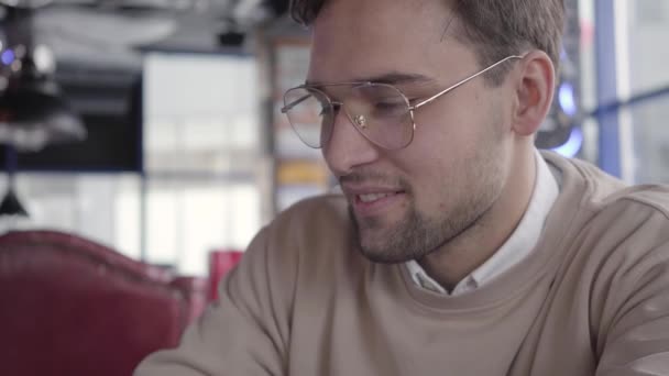 Retrato del hombre guapo mirando hacia abajo en la cafetería moderna de cerca. Elegante empresario confiado mueve su cabeza al ritmo de la música — Vídeo de stock