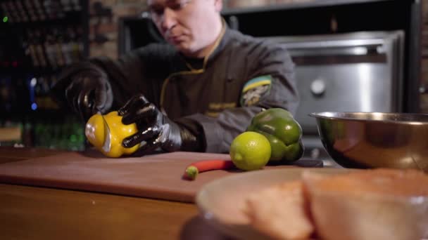 Portrét kuchař sekání s ostrým nožem zelené a žluté papriky na dřevěné desce připravit salát ve velký talíř — Stock video