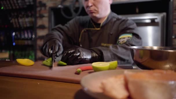 Cocinar profesional picando con cuchillo afilado pimiento verde y amarillo y lima en la tabla de madera para preparar ensalada en plato grande. De cerca. . — Vídeos de Stock