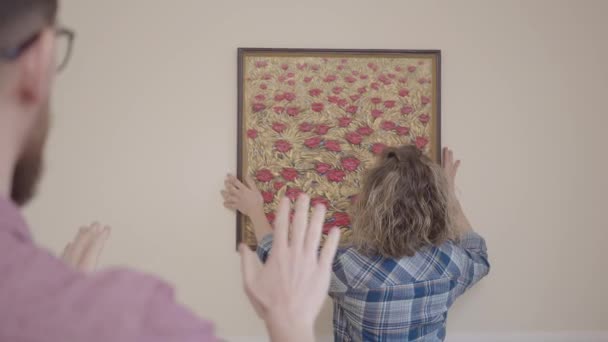 Husband tells his wife how to hang the picture on the wall correctly and according to the level. Young family moved to a new apartment. The concept of moving to a new home. — Stock Video