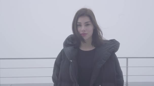 Portrait young pretty woman in black coat in cold autumn weather standing on the background of gray sky — Stock Video