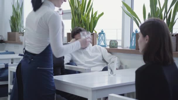 Los amigos están sentados en el restaurante, esperando la orden, y el camarero viene y trae vasos y una botella de agua — Vídeos de Stock