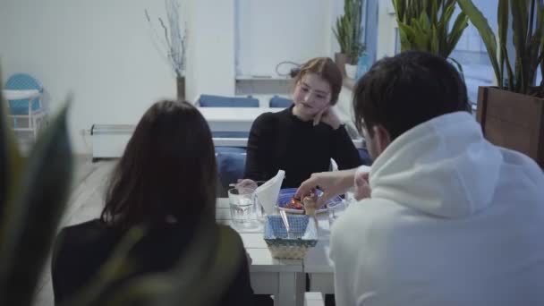 Una compañía de jóvenes está descansando en un acogedor restaurante o cafetería comiendo deliciosos platos para el almuerzo. — Vídeos de Stock