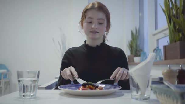 Porträtt av en cuteyoung rödhårig flicka äter i en vacker restaurang eller café. — Stockvideo