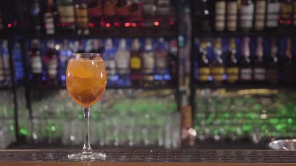 Жовтий коктейль у келиху з апельсином на барі. Пляшки алкоголю на фоні . — стокове відео