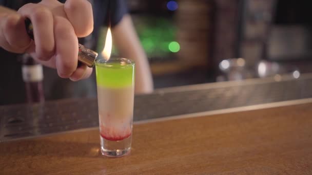 Bartender menempatkan api dari lebih ringan ke tembakan dengan lapisan warna berbeda alkohol di bar — Stok Video