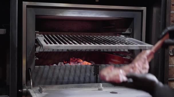 Les mains des chefs dans des gants noirs mettent un gros morceau de viande sur l'os à l'intérieur du four à charbon anal pour la cuisson — Video