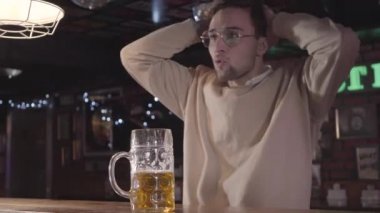 Çekici bir genç adam mutlu televizyonda futbol maç izlerken barda bira sahip gülümseyen yakın çekim. Barda yalnız alkol rahatlatıcı futbol takımı hayranıyım