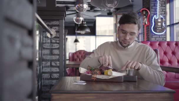Красивий хлопець сидить у розкішному ресторані та коментує чудову смачну страву з м'ясом та овочами на грилі — стокове відео