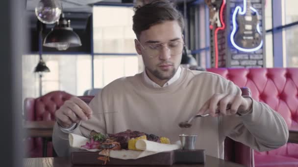 Knappe jongen zitten in luxe restaurant en eatting awesome heerlijke schotel met gegrild vlees en groenten — Stockvideo