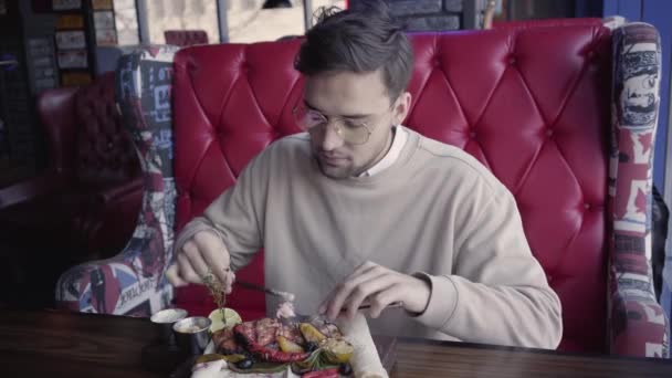 Красивый человек сидит в роскошном ресторане и ест удивительные вкусные блюда с жареным мясом и овощами — стоковое видео