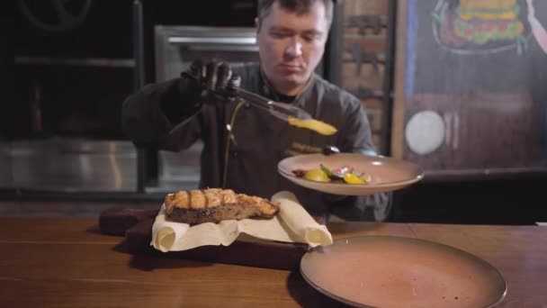 Chef en guantes negros que sirven en madera acaba de cocinar delicioso pescado jugoso con pimientos a la parrilla, chile picante y lima. De cerca. — Vídeos de Stock