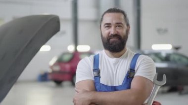 Bir İngiliz anahtarı konumu, kırık bir araba arka plan üzerinde bir oto tamircisi olan mekanik poz bir gülümseyen portresi sakallı.