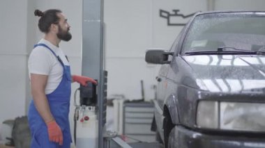 Yetişkin makinist otomatik Asansör kullanarak arabayı kaldırıyor. Alt araba Asansör Asansör düğmeye bas. Otomobil araba onarım istasyonu tespit yetenekli adam. Yan çekim