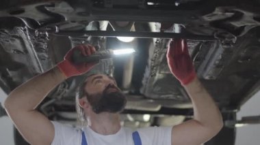 Profesyonel mekanik onarım servis istasyonunda lambalı teftiş sakallı. Arabayı tamir üniformalı usta erkeklere