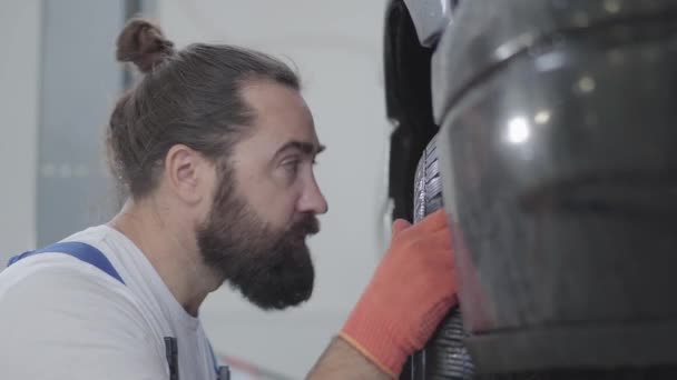 Portrait barbu mécanicien professionnel inspectant la suspension ou les freins dans la roue de voiture de l'automobile relevée à la station-service de réparation. Homme habile en uniforme de réparation de voiture — Video