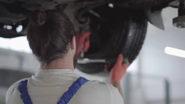 Ingeniero profesional atornillando los detalles del coche con una herramienta especial en el automóvil levantado en la estación de servicio de reparación de cerca. Un hombre hábil con guantes arreglando el coche. Servicio de coches, mantenimiento de reparación . — Vídeos de Stock