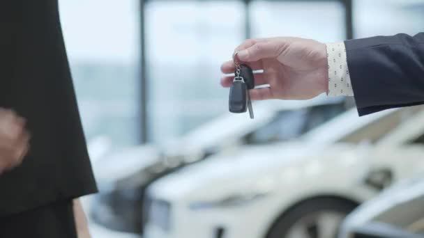 Mano masculina da las llaves de un coche a mano famale en el concesionario de automóviles de cerca. Vendedor de automóviles no reconocido y una mujer que compró un vehículo estrechan la mano . — Vídeos de Stock