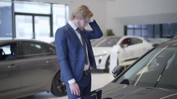 Bärtiger Geschäftsmann, der sein Auto im Autohaus aus nächster Nähe sucht. großer Mann läuft Hand durch Haare in der Nähe von Automobil in Auto Show-Raum, Blick auf Auto, Fahrzeug untersuchen. Kraftfahrzeug. — Stockvideo