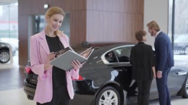 Araç seçimi çift önünde arabalar hakkında büyük bir kitapla pembe ceket hoş kadın portresi. Adam içinde kapı ve kadın oturur açar. Konsept otomobil, otomatik iş satın alma